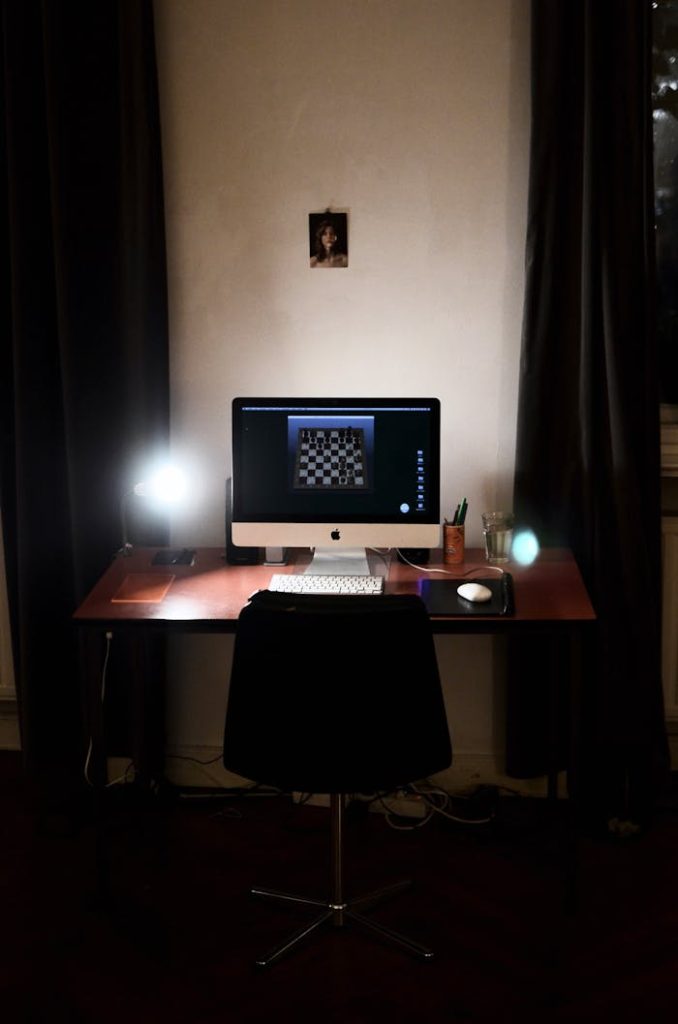 modern-computer-on-table-in-cabinet-6045099 A dimly lit workspace featuring a computer displaying a chess game with a sleek and modern aesthetic.